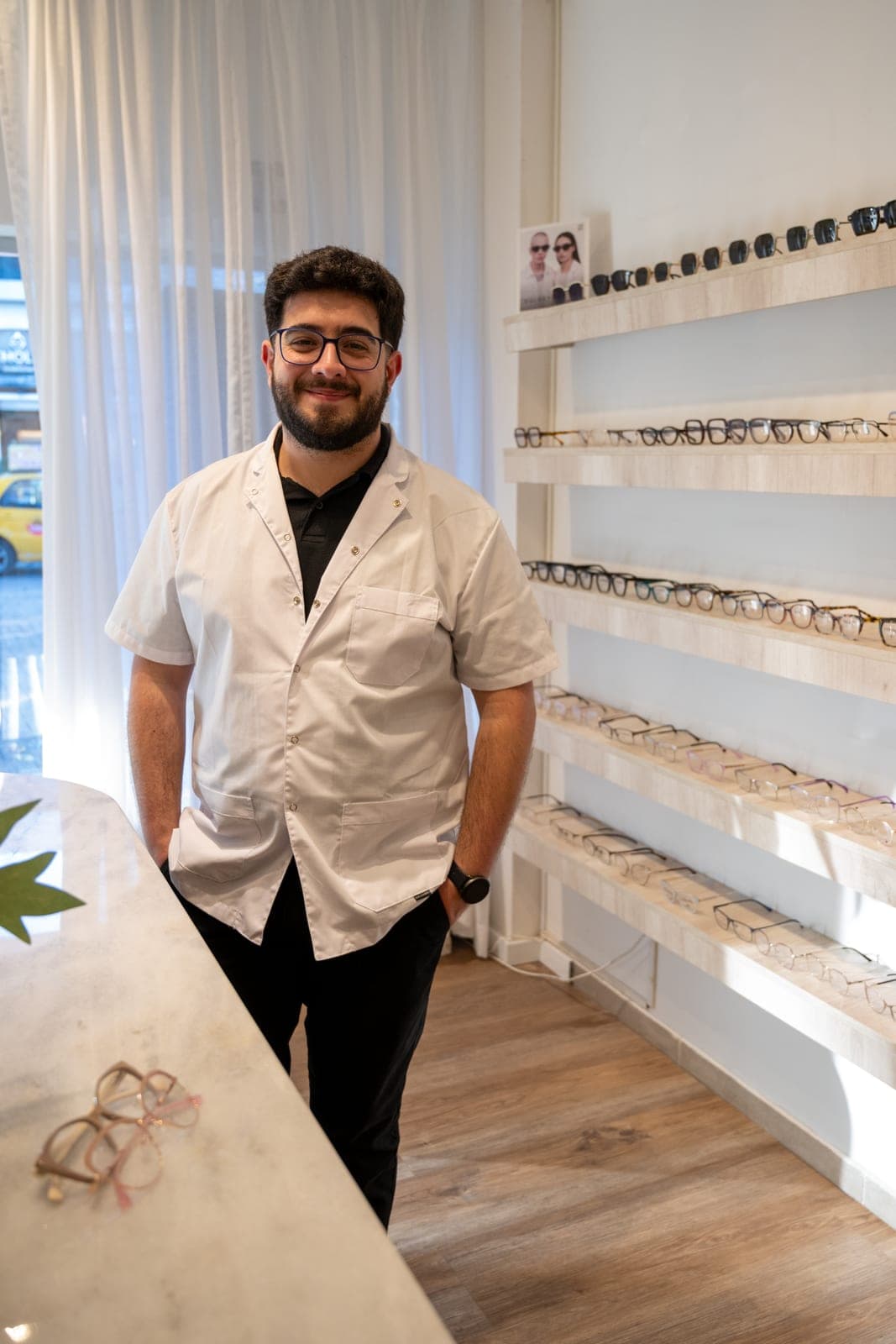 Matías, colaborador especializado de Atelier Óptica, junto a la pared de armazones